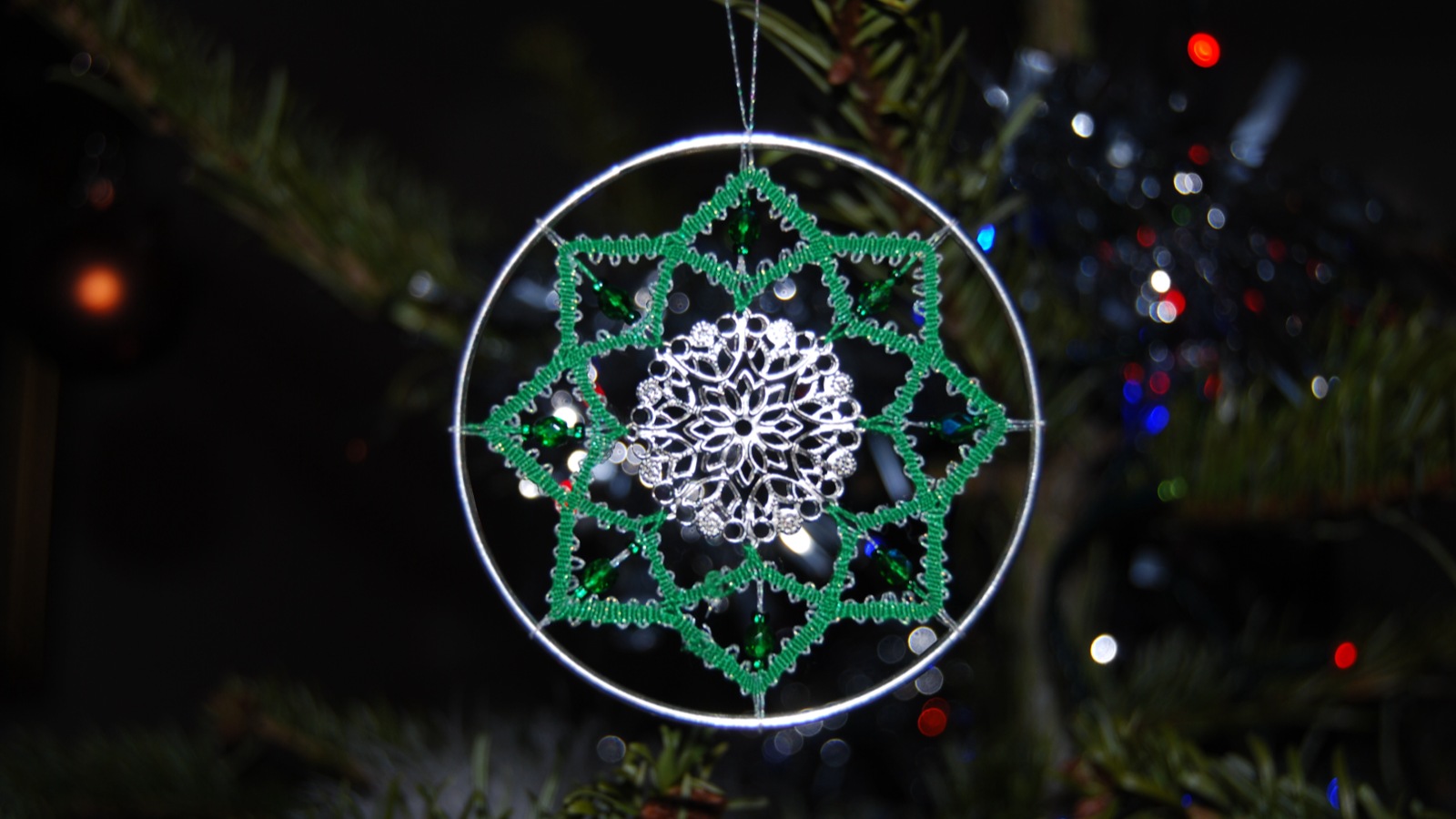 Green lace star with beads and a silver snowflake centre, hanging in a circular frame on a Christmas tree